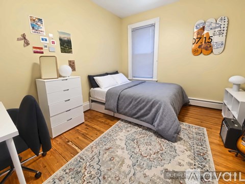 A bedroom with a bed, desk, chair, and a rug on the floor.