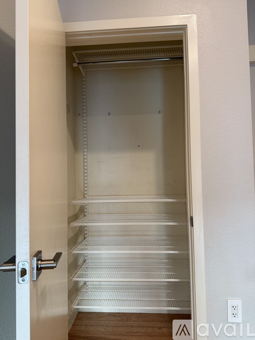A white door with a silver handle is open to a white interior with shelves.