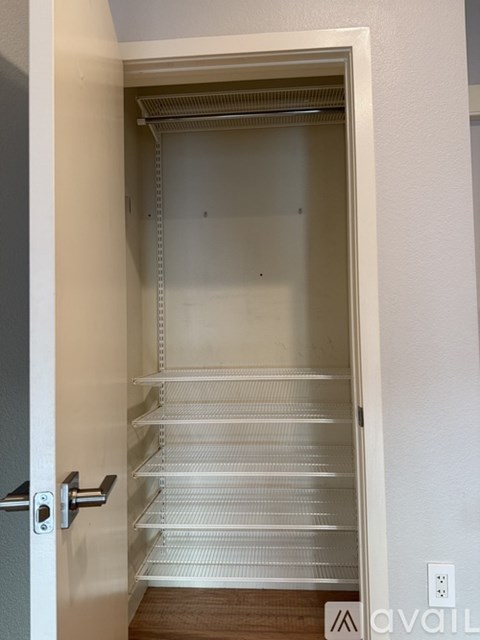 A white door with a silver handle is open to a white interior with shelves.