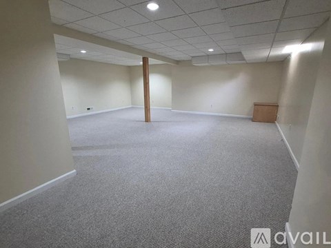 A spacious room with a carpeted floor and a wooden pillar in the middle.
