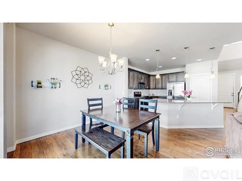 A dining room with a table and chairs and a kitchen in the background.