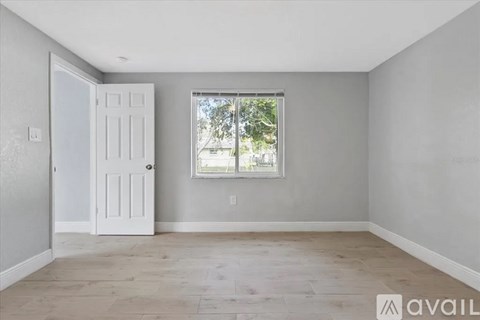 A room with a white door and a window with a view of trees outside.