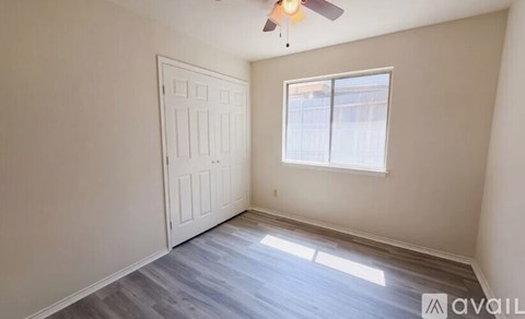 A room with a white door and a window with a fan on the ceiling.