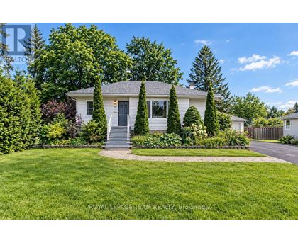 A white house with a grey roof and a grey front door is surrounded by greenery.