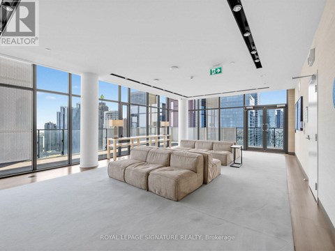 A spacious living room with a large sectional sofa and a view of the city through the windows.