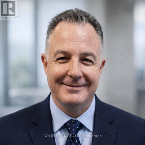 A man in a suit with a dotted tie smiles at the camera.