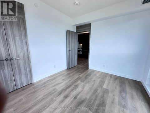 A room with a wooden floor and a white wall with a doorway leading to another room.