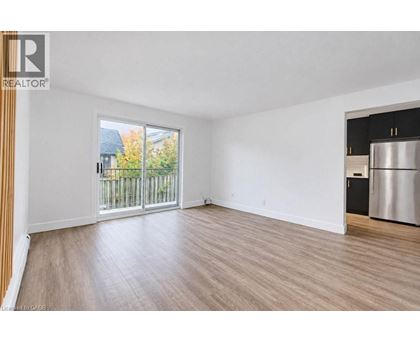 A spacious room with a wooden floor and a large window overlooking a fence.