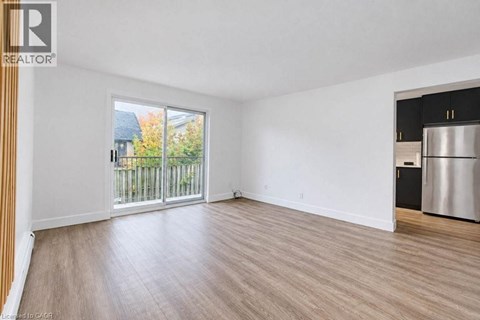 A spacious room with a wooden floor and a large window overlooking a fence.