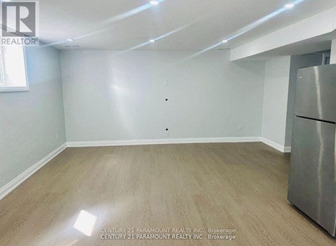 A spacious room with light wood flooring and a stainless steel refrigerator.