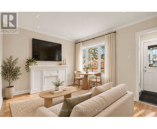 A living room with a white fireplace, a flat screen TV mounted on the wall, and a large window with curtains.