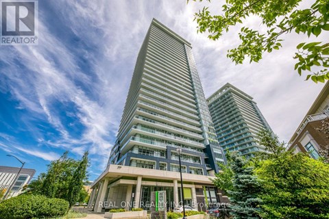 A modern building with a triangular top is surrounded by greenery and other buildings.