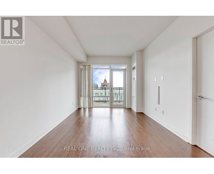 A spacious room with wooden floors and a view of a cityscape through the windows.