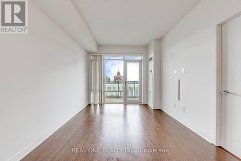 A spacious room with wooden floors and a view of a cityscape through the windows.