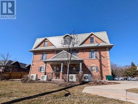 A large brick house with a porch and a tree in front.