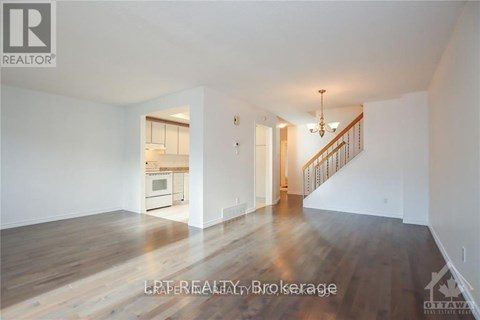A spacious room with wooden floors and a staircase leading to another room.