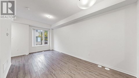 A spacious room with wooden flooring and a window showing a view of trees and a building.