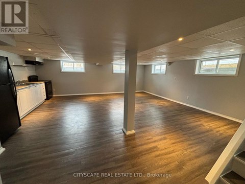 A spacious room with wooden flooring and white walls, with a black refrigerator on the left side.