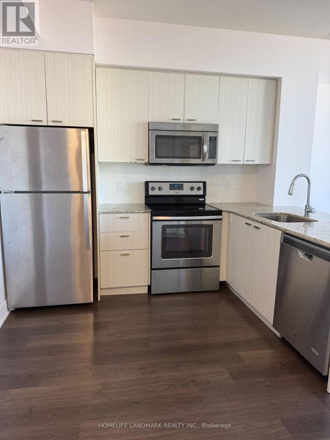 A kitchen with a refrigerator, microwave, oven, and sink.