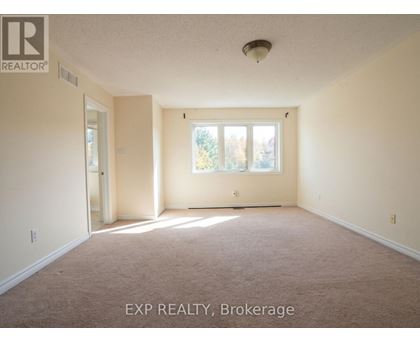 A room with a carpet floor and a window with a view of trees.
