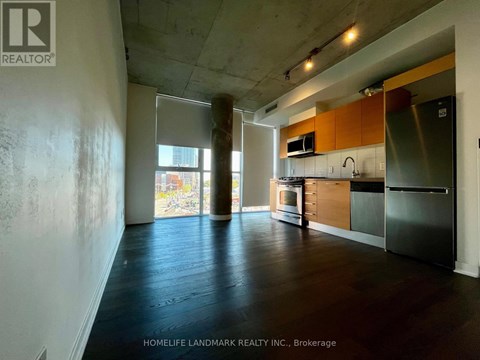 A kitchen area with wooden floors and a stainless steel refrigerator.