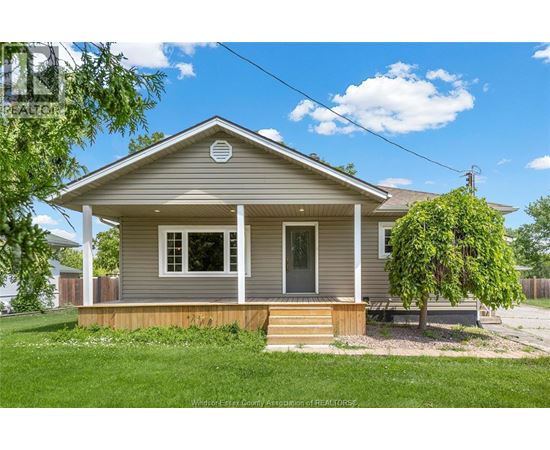 A small house with a porch and a tree in front.