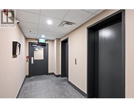 A hallway with a black door on the right and a black door with a red sign on the left.