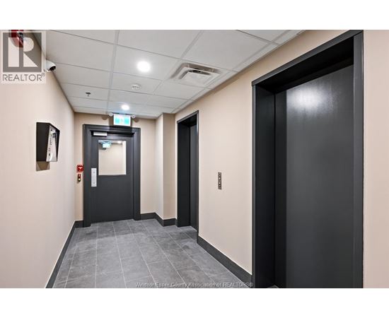 A hallway with a black door on the right and a black door with a red sign on the left.