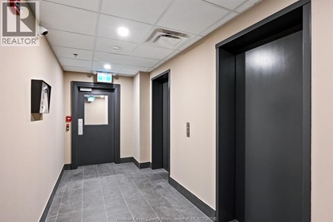 A hallway with a black door on the right and a black door with a red sign on the left.