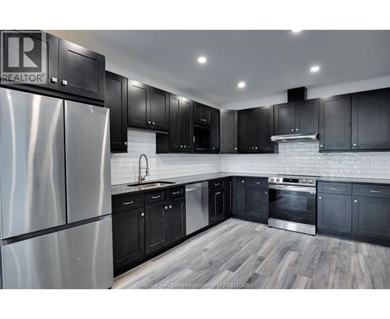 A kitchen with black cabinets and a stainless steel refrigerator.