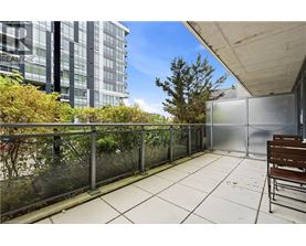 A balcony with a bench and a glass railing overlooking a tree and a building.