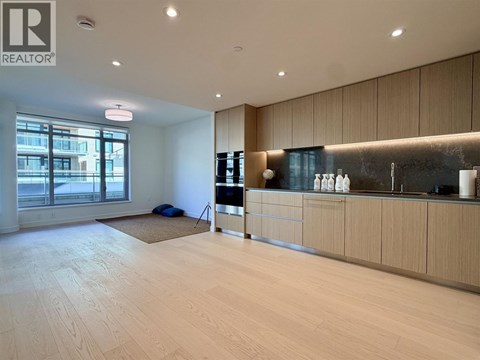 A spacious room with wooden flooring and a kitchen area with a sink and cabinets.