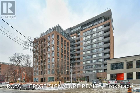 A modern multi-story building with a glass facade stands in front of a tree-lined street.
