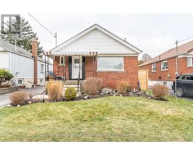 A brick house with a white door and windows is surrounded by a grassy front yard.