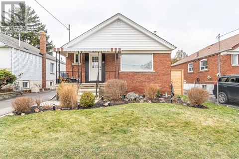A brick house with a white door and windows is surrounded by a grassy front yard.