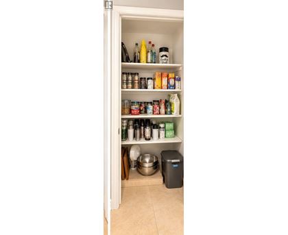 A kitchen pantry with a variety of food items and a trash can.
