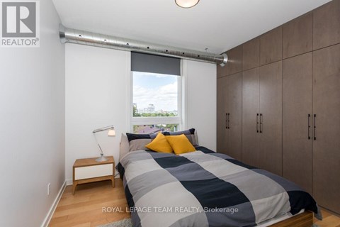 A bedroom with a bed, nightstand, and a window with a view of the city.