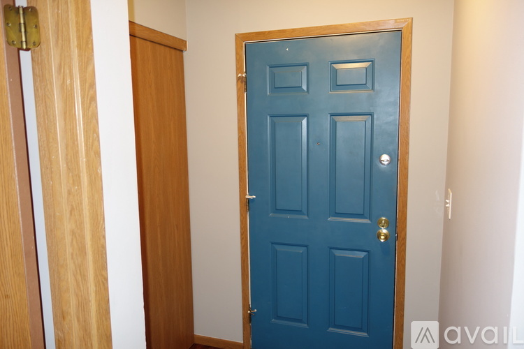 A blue door with a brass handle is in a white hallway.
