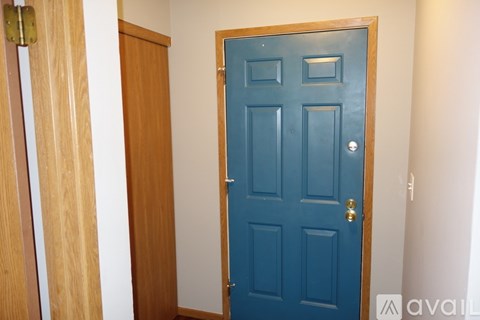 A blue door with a brass handle is in a white hallway.