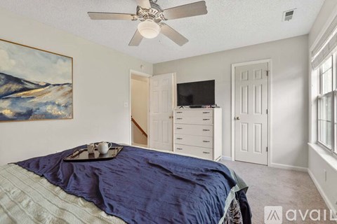 A bedroom with a bed, a ceiling fan, and a painting on the wall.