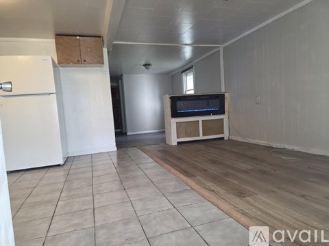 A spacious room with a white refrigerator, a wooden entertainment center, and a tiled floor.