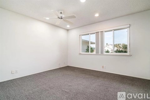 A room with a ceiling fan and a window overlooking a building.
