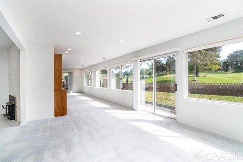 A spacious, empty room with a fireplace and large windows overlooking a grassy area.