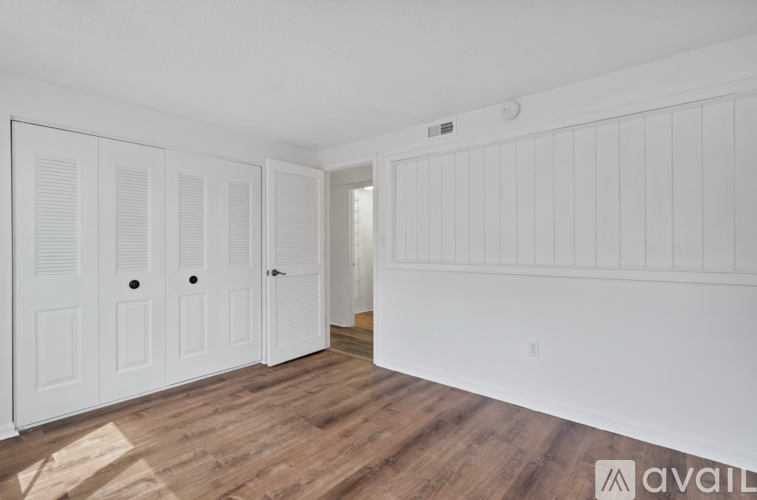A room with white walls and wooden flooring, featuring a white door with a black handle and a small window above it.