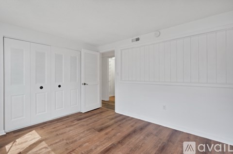 A room with white walls and wooden flooring, featuring a white door with a black handle and a small window above it.