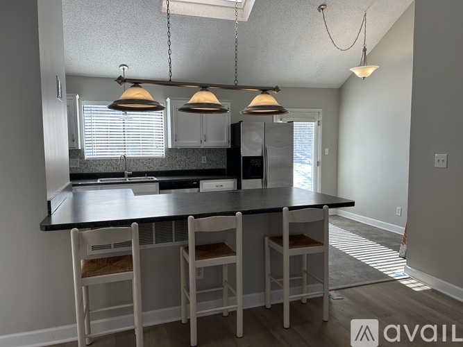 A kitchen with a black countertop and white chairs.