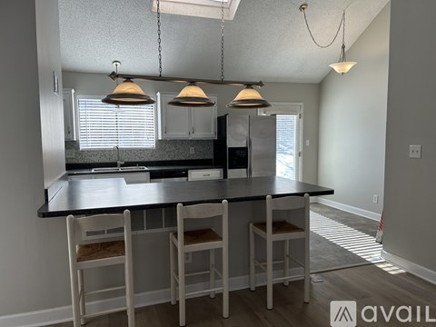 A kitchen with a black countertop and white chairs.