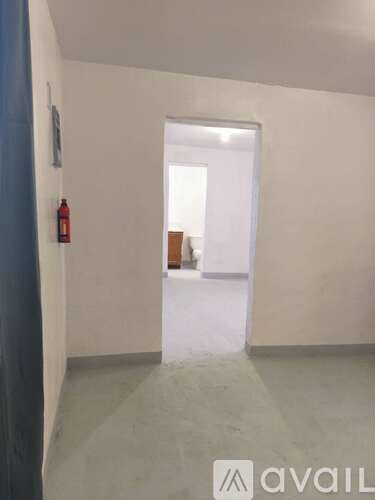 A room with a fire extinguisher on the wall and a doorway leading to another room.