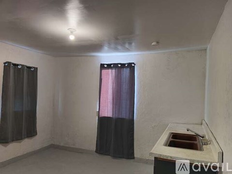 A room with a sink and two windows with curtains.