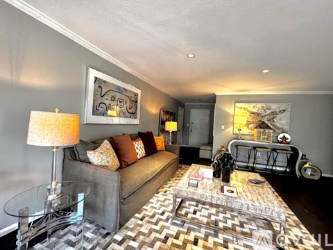 A living room with a grey couch, a glass coffee table, and a large painting on the wall.